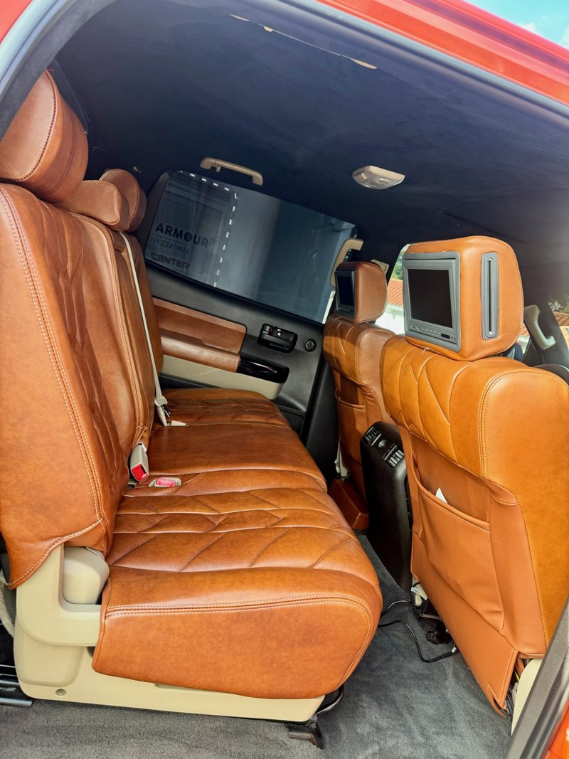Brown leather SUV back seat with fold-down headrest screens and beige interior trim.