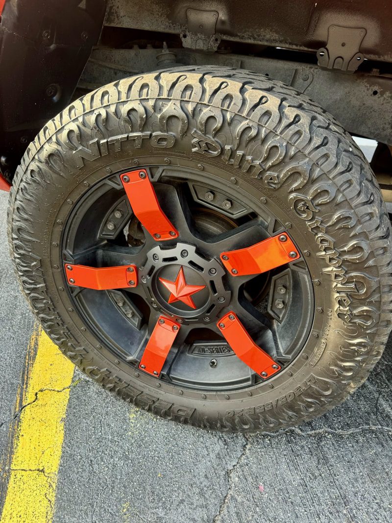 Off-road wheel with black five-spoke rim and bright orange mounting brackets, star center cap, mounted on a rugged treaded tire.
