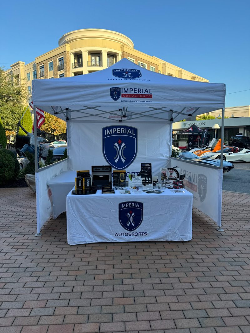 White event tent for Imperial Autosports with table of products and brand logos in a plaza setting.