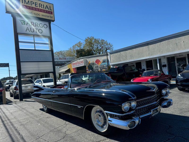 Shiny black vintage convertible with white-wall tires parked outside an auto shop on a sunny day.