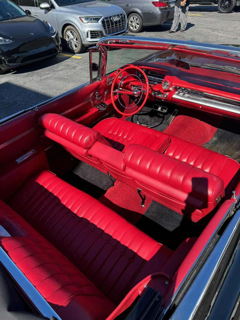 Red vintage convertible interior with red leather seats, chrome dashboard and steering wheel, parked in a car lot.