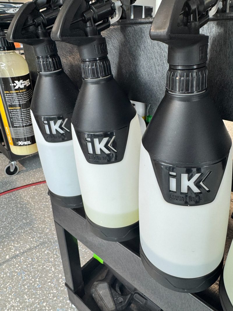 Three IK spray bottles on a workshop rack, used for car detailing image.