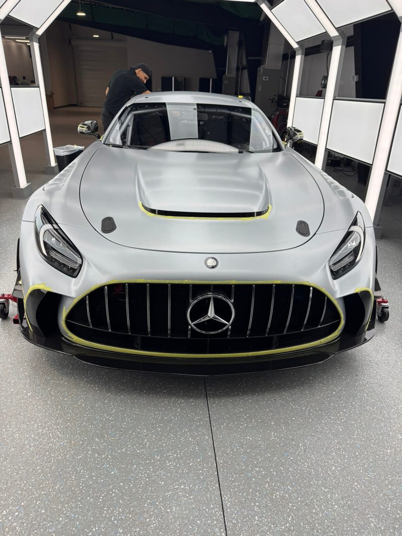 Front view of a silver Mercedes sports car in a workshop, with yellow masking tape along the hood and grille edges.