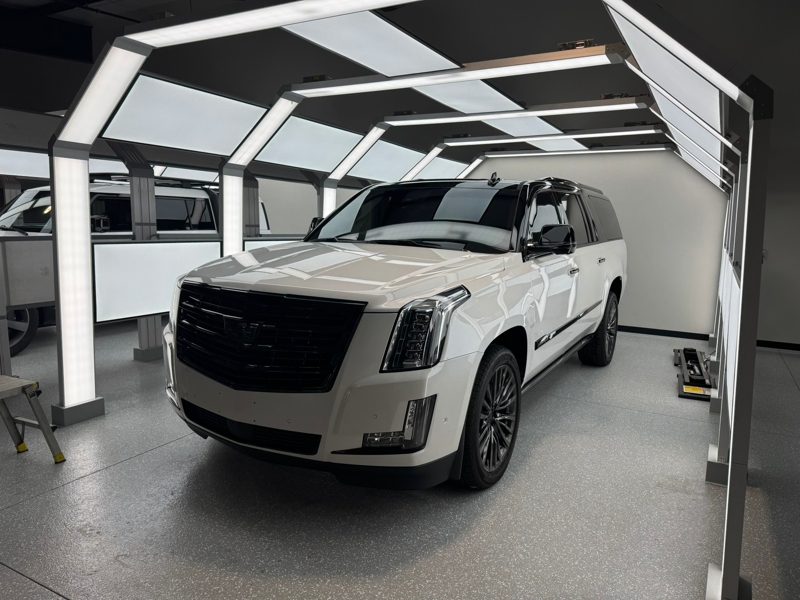 White luxury SUV inside a bright photo studio with framed overhead lighting rigs.