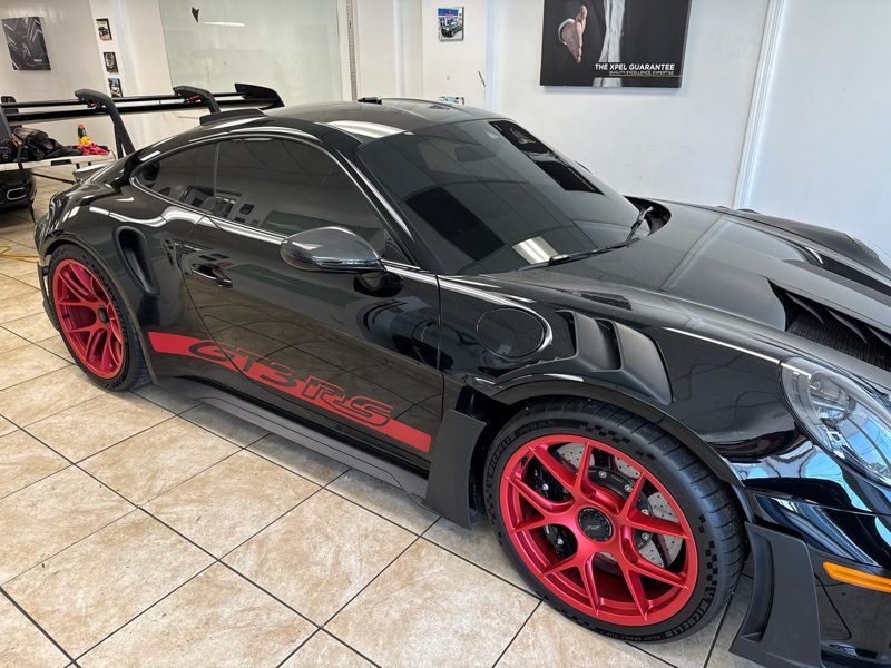 Black Porsche GT3 RS in a showroom with red alloy wheels and a red side decal on the door.