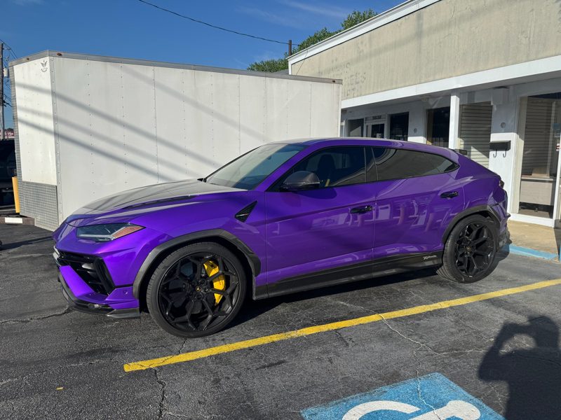Purple high-performance SUV with black wheels and yellow brake calipers parked in a lot beside a white trailer.