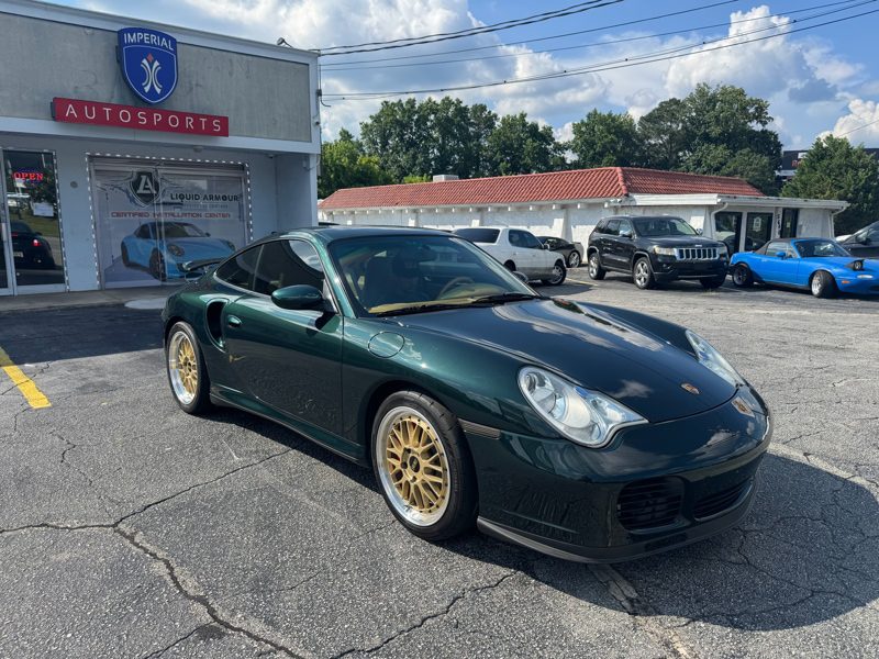 Dark green Porsche 911 with gold wheels parked in front of Imperial Autosports showroom; other cars visible in the lot.