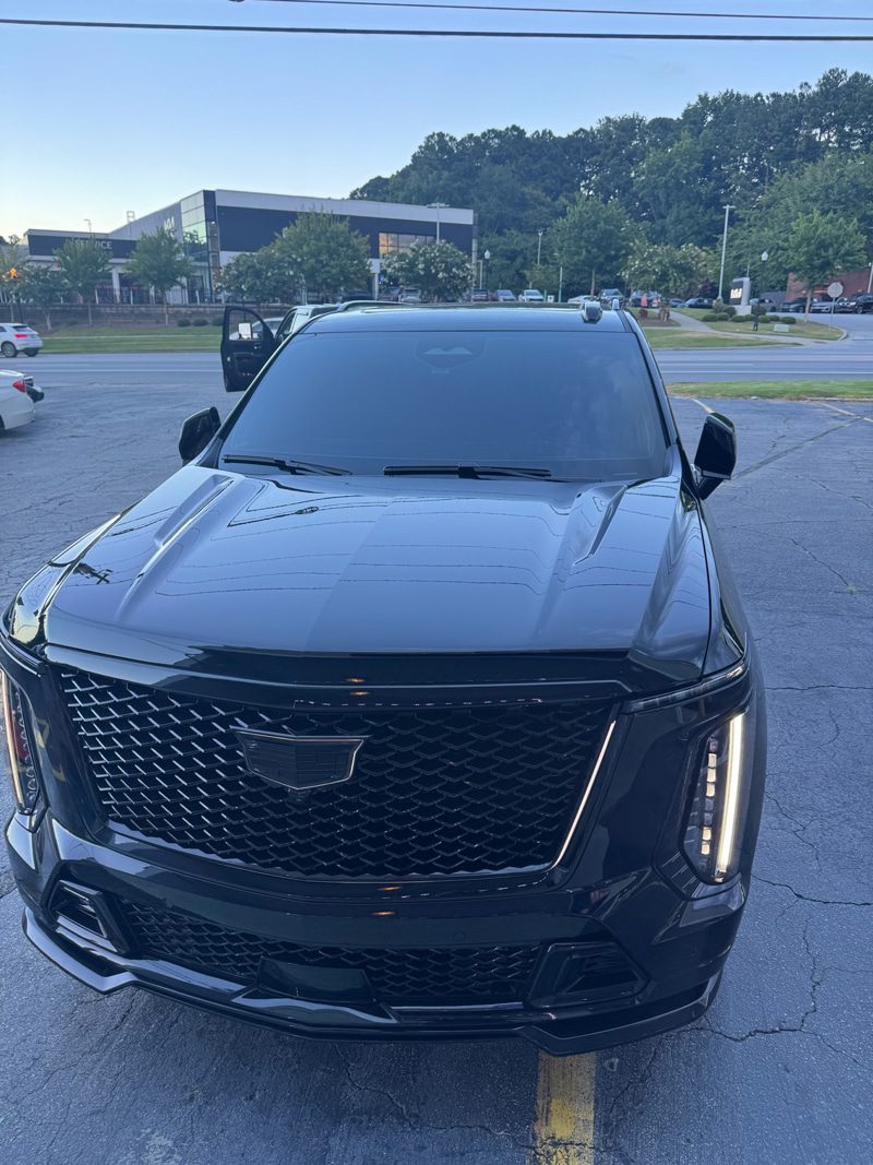 Front view of a black SUV with a large mesh grille and vertical LED headlights in a parking lot, driver's door open.