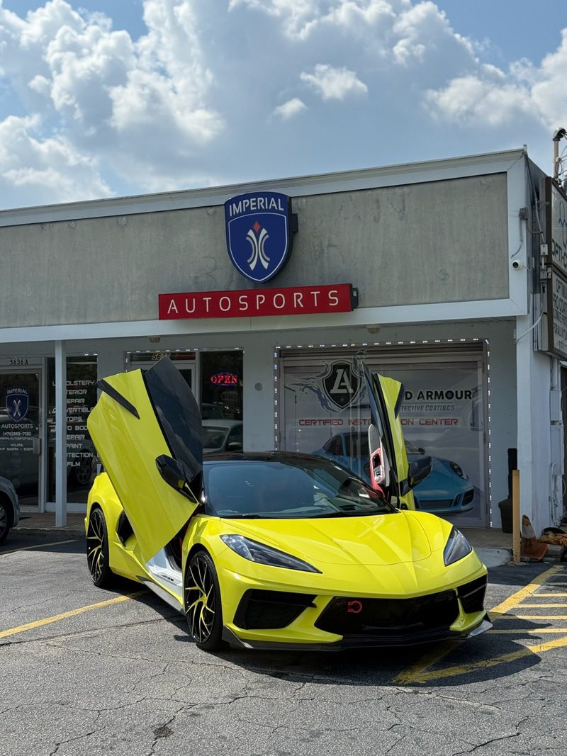 Bright yellow sports car with scissor doors open in front of Imperial Autosports shop signage