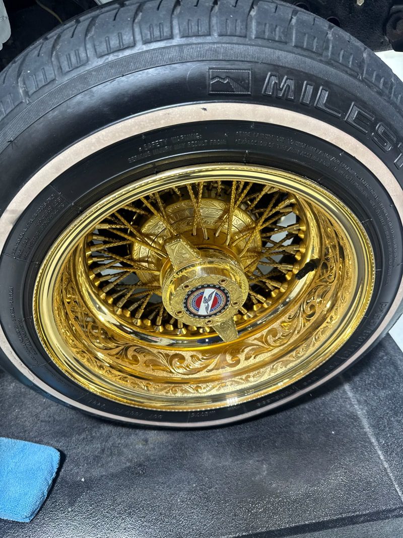 Gold ornate wire-spoke car wheel with a detailed engraved rim and center cap