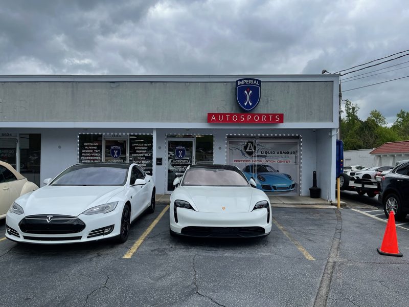 White cars parked in front of the Imperial Autosports storefront with a blue shield logo and red Autosports sign.