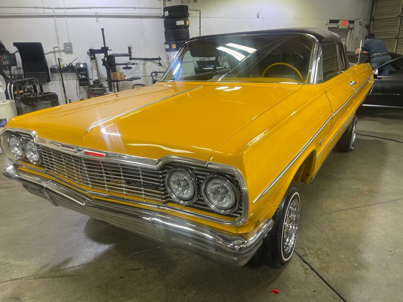 Front three-quarter view of a yellow vintage Chevrolet Chevelle convertible with a black soft top parked in a workshop.