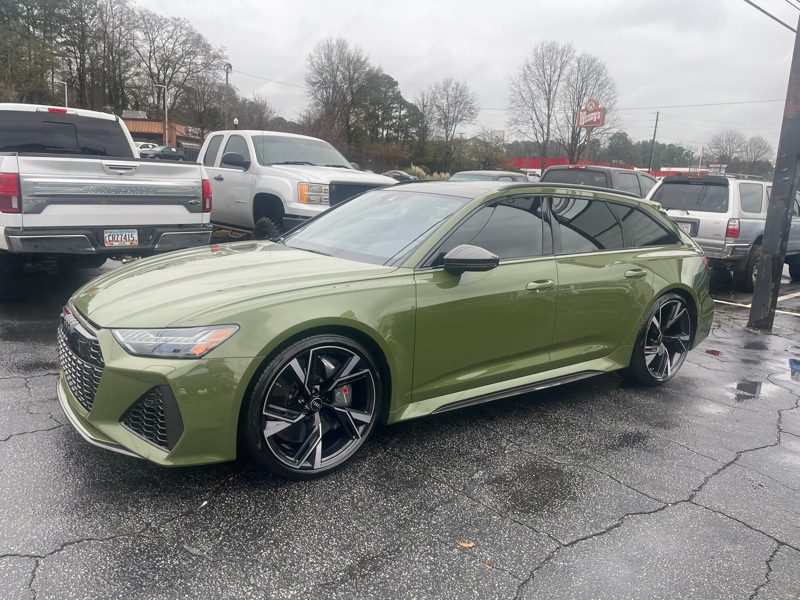 Green sedan with black alloy wheels parked in a wet parking lot, front three-quarter view from the driver's side surface detail visible.