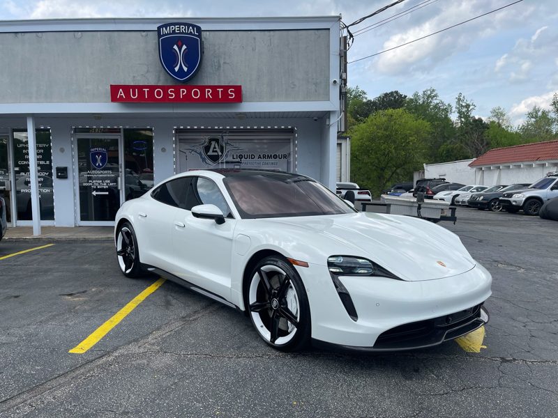 White Porsche Taycan parked in front of Imperial Autosports with the dealership facade and red Autosports sign in view
