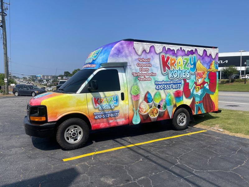 Colorful ice cream truck with Krayz Kones branding parked in a lot, featuring ice cream graphics and a cartoon mascot on the side.