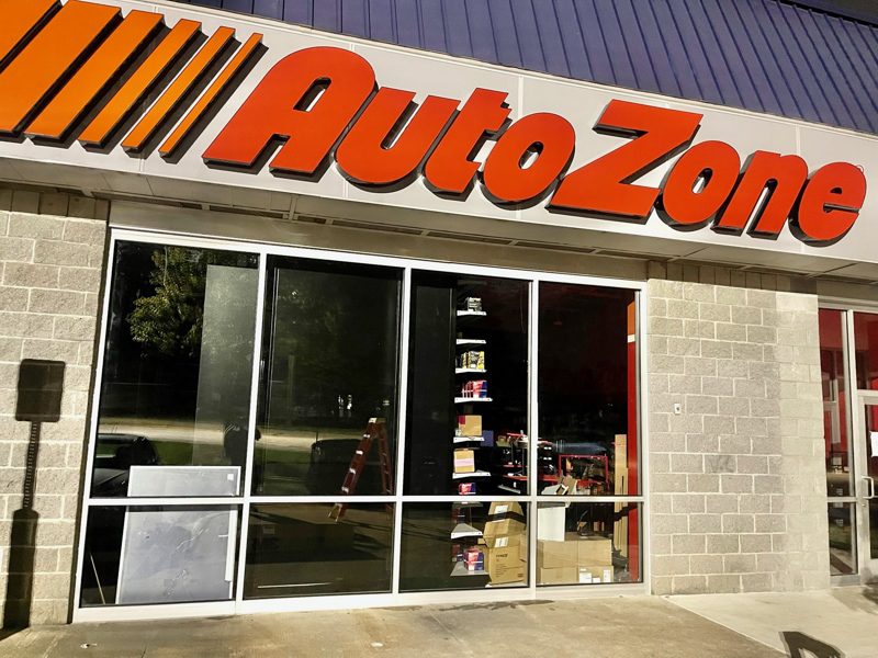 AutoZone storefront with large orange sign, glass windows, and stored goods visible inside the entrance area.