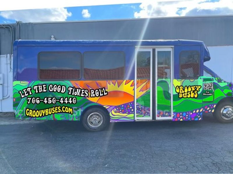 Colorful graffiti-painted bus with the slogan 'Let the Good Times Roll,' a phone number 706-450-4446, the site groovybuses.com, and a 'Groovy Buses' logo on the side.